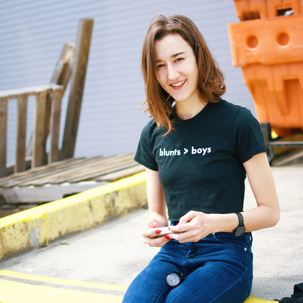 Woman smiling in a black crop top that reads blunts > boys in white letters